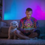 Man chilling on sofa with dog reading, wearing wearing Alex Tooth Radiant Bloom Long Sleeved Balance Tee T-Shirt.