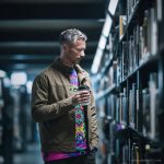 Man in a library browsing books, wearing wearing Alex Tooth Radiant Bloom Long Sleeved Balance Tee T-Shirt.