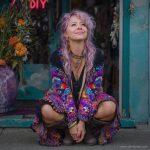 Alternative looking hippy woman sitting outside smiling, wearing long zip up fleece lined Alex Tooth Inner Flight Ritual Robe