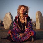 Alternative looking hippy woman sitting outside smiling, wearing long zip up fleece lined Alex Tooth Inner Flight Ritual Robe