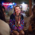 Alternative looking hippy woman sitting outside smiling, wearing long zip up fleece lined Alex Tooth Inner Flight Ritual Robe