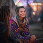 Alternative looking hippy woman sitting outside smiling, wearing long zip up fleece lined Alex Tooth Radiant Bloom Ritual Robe