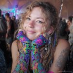 Alternative looking hippy style woman smiling, wearing Alex Tooth Radiant Bloom Aurasleeve Gloves.