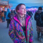 Alternative looking hippy style woman in a winter season outdoor setting wearing an Alex Tooth Radiant Bloom Nomad Coat Long Puffer Winter Coat.