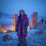 Alternative looking hippy style woman in a winter season outdoor setting wearing an Alex Tooth Radiant Bloom Nomad Coat Long Puffer Winter Coat.